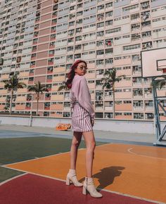 a woman standing on a basketball court in front of a tall building with balconies