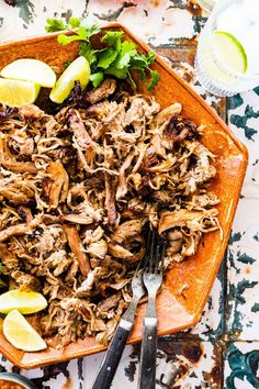 a plate full of shredded meat and garnished with cilantro, limes, and lemon wedges