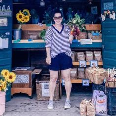 a woman standing in front of a store with sunflowers