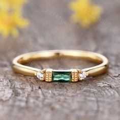 an emerald and diamond ring sitting on top of a piece of wood with flowers in the background