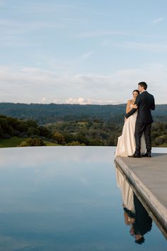 a bride and groom standing on the edge of a pool