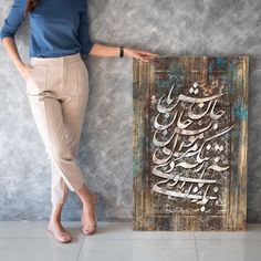 a woman standing next to a painting with an arabic calligraphy written in silver on it