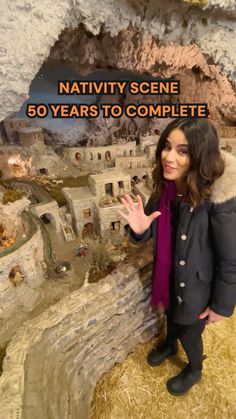 a woman standing in front of a fake model of a town with text that reads nativity scene 60 years to complete