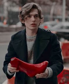 a man holding a pair of red shoes in his hands while walking down the street