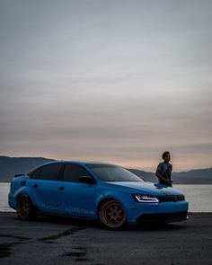 a man standing next to a blue car near the water