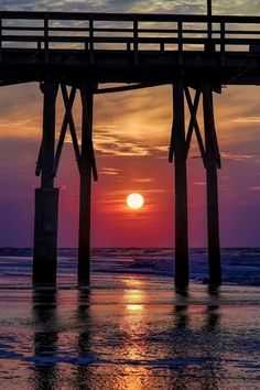 the sun is setting over the ocean with a pier in the foreground and water below it