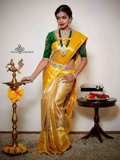 a woman in a yellow and green saree standing next to a small table with food on it