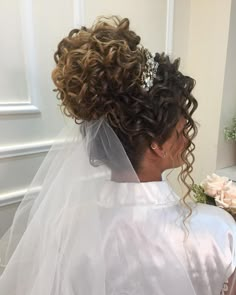 a woman with curly hair wearing a wedding veil and holding a bouquet in her hand