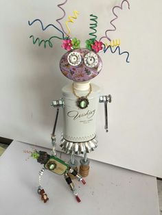 a robot made out of various objects on top of a white table next to a wall