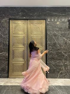 a woman in a long pink dress is walking by a door with her arms outstretched