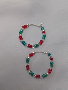 A pair of red, silver lined and green glass seed bead earrings, with a silver 'stopper bead' at the end to stop them easily slipping off the silver hoop.  The hoop has a diameter of approx. 2.3cm. these are quite delicate hoops so care must be taken when putting in and taking out. A fun, festive pair of unique, handmade earrings, with a Christmassy style, ideal for the festive time of year. I can also make in alternative colour combinations if needed, just send me a message with your requirements! To keep your jewellery in the best condition for the longest period, please note:  - Remove jewellery before bathing, showering or swimming.  - Avoid direct contact with body lotions, perfumes and any other chemicals. - Remove jewellery before sleeping. - When not in use, store jewellery in it's Holiday Jewelry With Colorful Red Beads, Holiday Red Jewelry With Colorful Beads, Red Christmas Jewelry With Colorful Beads, Gift Dangle Hoop Earrings With Spacer Beads, Small Hoop Beaded Earrings With Spacer Beads For Gifts, Small Hoop Beaded Earrings With Spacer Beads As Gift, Handmade Round Jewelry For Christmas, Handmade Round Christmas Jewelry, Handmade Round Beads Jewelry For Holiday