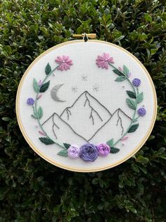 a cross stitch pattern with mountains and flowers in the middle, surrounded by greenery