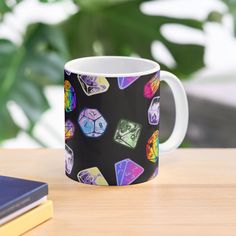 a coffee mug with colorful dice on it sitting on a table next to a book