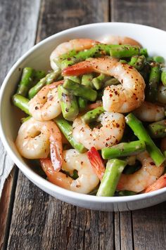 a white bowl filled with shrimp and asparagus on top of a wooden table