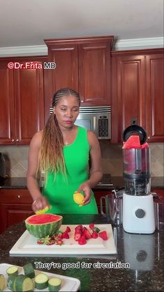 a woman in a green dress is cutting fruit on a counter top with a blender