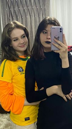 two young women taking a selfie in front of a mirror with their cell phones