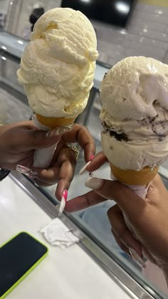 two ice cream cones are being held up by someone's hands in front of a mirror