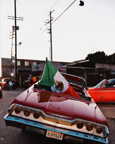 an old red car with a mexican flag on it's hood parked in the street