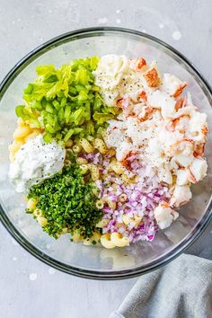 a glass bowl filled with different types of vegetables and seasoning next to a gray towel