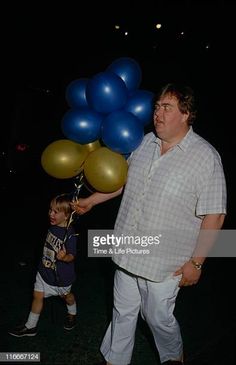 a man holding balloons with a little boy standing next to him in the dark at night