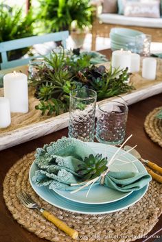 a place setting with succulents, candles and glassware on the table