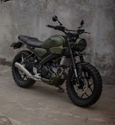 a green motorcycle parked in front of a cement wall with graffiti on it's side