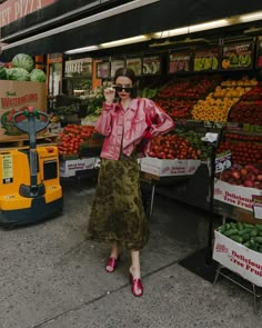 a woman standing in front of a fruit stand talking on her cell phone while wearing pink shoes