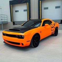 an orange and black sports car parked in front of two garage doors with one door open