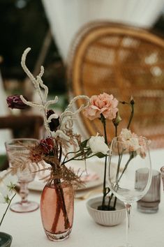 flowers are in vases on a table with wine glasses and plates around it,