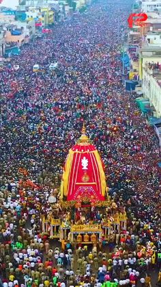 a large group of people standing in front of a red and yellow building with a statue on top