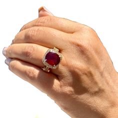 a woman's hand holding a ring with a large red stone in the middle