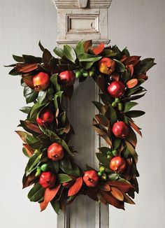 a wreath is hanging on the door with apples and leaves around it in front of an old window