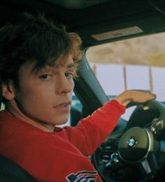 a young man sitting in the driver's seat of a car with his hand on the steering wheel