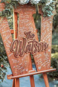 a wooden easel with writing on it and flowers in the top right hand corner