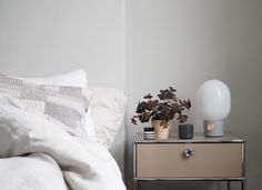 a white bed sitting next to a nightstand with a plant on top of it in a bedroom