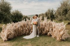 a bride and groom are standing in front of some tall grass with flowers on it