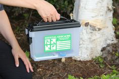 a person holding a plastic container in their hand next to a tree and shrubbery