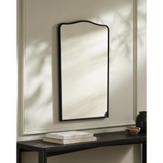 a mirror sitting on top of a wooden table next to a wall mounted shelf with a book