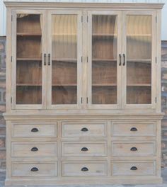 an old white china cabinet with glass doors and drawers on the bottom shelf, in front of a brick wall