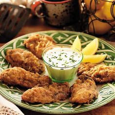 fried chicken with ranch dressing on a green and white plate next to lemon wedges