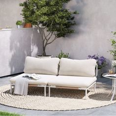 a white couch sitting on top of a rug next to a table and potted plant