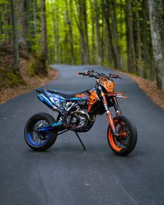 an orange and blue dirt bike parked on the side of a road in front of trees