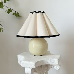 a table lamp sitting on top of a white pedestal next to a potted plant