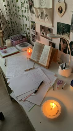 an open book sitting on top of a table next to a candle and some pictures