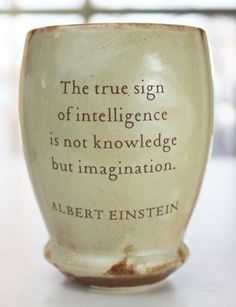 a coffee cup with the words albert einstein on it sitting on a white table in front of a window