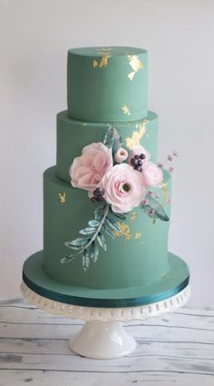 a three tiered green cake with pink flowers on the top and gold leaf decorations