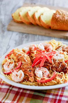 a white plate topped with pasta covered in shrimp and tomato sauce next to sliced loaves of bread