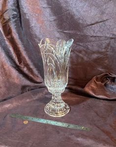 a clear glass vase sitting on top of a brown cloth covered table next to a ruler