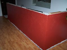 a red wall in the middle of a room with wood flooring and a mirror above it