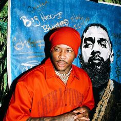 a man in an orange shirt and hat standing next to a painting of a bearded man